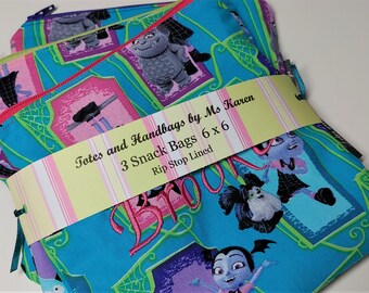 May include: Three teal snack bags with a colorful cartoon print featuring characters and the word "BOOOM". Each bag has a pink zipper and is labeled "Totes and Handbags by Ms Karen 6 x 6".