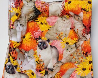 May include: Quilted fabric item featuring a vibrant pattern of cats and flowers. The design includes various cat breeds amidst yellow, orange, and pink flowers. The item is quilted with red thread, creating a textured appearance.