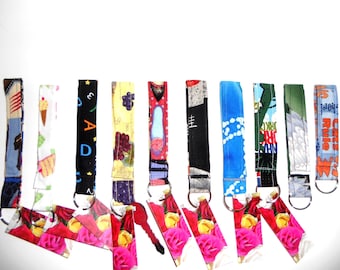 May include: A collection of ten fabric wristlet keychains featuring various patterns including ice cream cones, alphabet letters, grapes, floral motifs, and text such as Cats Rule. Each strap is attached to a silver metal split ring.