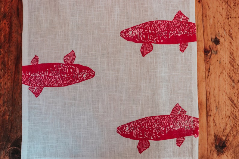 May include: A white linen tea towel with a red fish design. The fish are printed in a simple, blocky style.