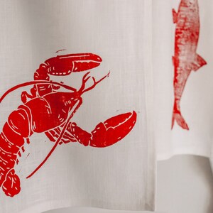 May include: A white kitchen towel with a red lobster print. The lobster is in a curled position with its claws raised.