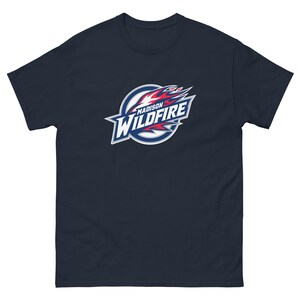 May include: Navy blue t-shirt featuring the Madison Wildfire logo. The logo is a stylized design with a flame motif in red, white, and blue, set against a white and blue circle. The text "MADISON WILDFIRE" is prominently displayed.