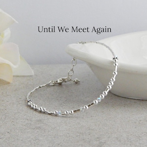 May include: A delicate silver-toned bracelet featuring a series of small metallic beads and tiny clear crystals. The bracelet includes a lobster claw clasp and an adjustable chain. The text "Until We Meet Again" is printed above the jewelry piece.