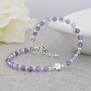May include: A delicate amethyst gemstone bracelet with a silver flower charm. The bracelet is made with small, round amethyst beads and silver spacer beads.