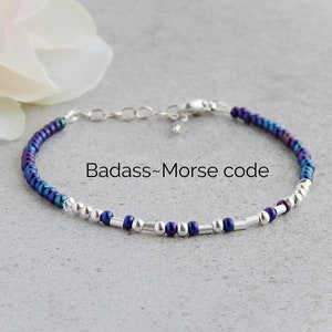 May include: A beaded bracelet with iridescent blue and silver beads. The bracelet has a silver clasp and a small crystal charm. The bracelet is on a gray background. "Badass-Morse code" is written in white text on the background.