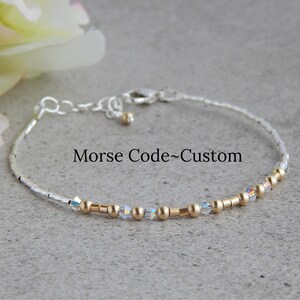 May include: A silver bracelet with gold beads and clear crystals. The bracelet has the text "Morse Code-Custom" on it.