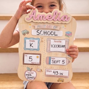 Könnte beinhalten: Ein helles Holzschild für den ersten Schultag mit dem Namen Amelia in rosa Schreibschrift. Das Schild enthält Bereiche für die Klasse K, Lieblingseis, Alter 5, Datum 5. Sept., Lehrerin Frau Jones und eine Körpergröße von 43 Zoll.