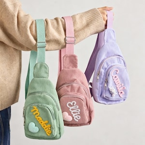May include: Three corduroy sling bags in mint green, dusty pink, and lavender. Each bag features an adjustable woven strap, a front zippered pocket, and a personalized name patch in cursive script with a small heart or flower applique.