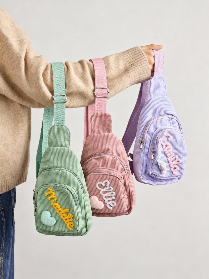 May include: Three corduroy sling bags in mint green, dusty pink, and lavender. Each bag features an adjustable woven strap, a front zippered pocket, and a personalized name patch in cursive script with a small heart or flower applique.