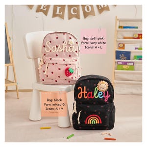 Op de afbeelding: Twee gepersonaliseerde rugzakken. E&eacute;n is zachtroze met een aardbei en de naam "Sasha". De andere is zwart met de naam "Haley" en een regenboog. Beide hebben stippen. De rugzakken staan op een witte stoel.