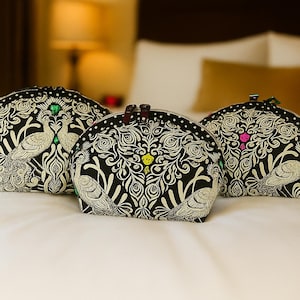 May include: Three black cosmetic bags with a white peacock and floral design. The bags have a rounded shape and a zipper closure. The bags are on a white surface.