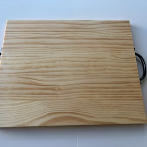 May include: A rectangular wooden serving tray with a light wood grain pattern. The tray has black metal handles on each side. The wood has a natural, light brown color.