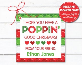 Op de afbeelding: Een printbare kerstcadeau-tag met een rood, groen en wit pop-it speelgoedontwerp. De tag zegt "Ik hoop dat je een knallend kerstfeest hebt! Van je vriend, [Naam]"