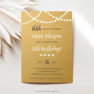 May include: Gold invitation with a string of white lights at the top. The text reads "shhh... help us surprise Susan Johnson and celebrate her 70th birthday!"  Oct. 26, 2024. At 6 o'clock in the evening at Flemings on First, 528 First Street, Washington. Please RSVP to Kelly by October 20th, (555) 555-5555. www.LilyGirlPaper.Etsy.com