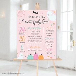 May include: A pink and white printable sign with a ghost and pumpkins. The sign says "Caroline is a Sweet Spooky One!" and includes details about the child's age, weight, height, and favorite things.