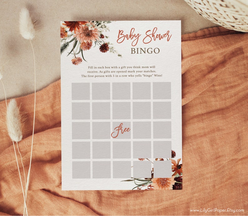 Może przedstawiać: Drukowana karta do gry w bingo na baby shower z kwiatowym wzorem w odcieniach pomarańczowego i brązowego. Karta ma siatkę 25 kwadrat&oacute;w z napisem "Free" w środkowym kwadracie. Tekst "Baby Shower Bingo" znajduje się na g&oacute;rze karty.
