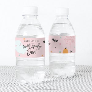 May include: Pink and white water bottle labels with a ghost, bats, a spider, a pumpkin, and candy corn. The text on the label reads "Caroline is sweet spooky one!"
