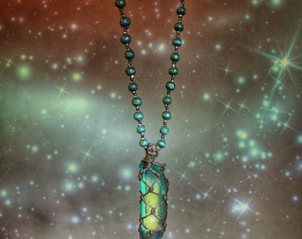 May include: A green crystal pendant wrapped in wire hangs from a beaded necklace. The necklace is made of dark green beads and the pendant is a long, thin crystal with a light green hue.