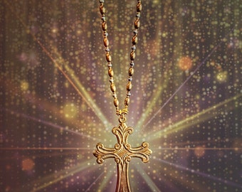 May include: A gold cross pendant necklace with a detailed design hangs on a chain against a sparkling background.