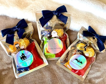 May include: Three clear cellophane bags filled with candy and treats, each tied with a navy blue bow. Each bag has a holographic sticker with a Halloween theme and the words "Happy Halloween".