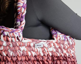 Może przedstawiać: Torba na ramię wykonana na szydełku w odcieniach różowego, białego i fioletowego. Torba ma metkę z napisem "Malaine".