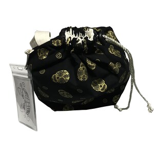 May include: Black drawstring bag with a gold sugar skull pattern. The bag has a white drawstring and a clear plastic ID holder attached.