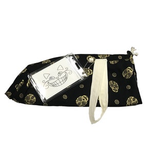 May include: Black drawstring bag with a gold skull pattern. A clear plastic pouch with a black and white illustration of a cat with a wide grin is attached to the bag.