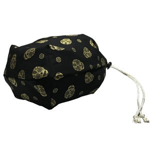 May include: Black drawstring bag with a white cord. The bag is decorated with a repeating pattern of gold sugar skulls.