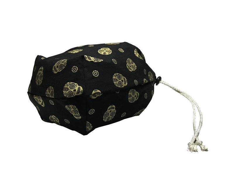 May include: Black drawstring bag with a white cord. The bag is decorated with a repeating pattern of gold sugar skulls.