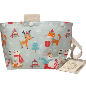 May include: A light blue fabric tote bag with a Christmas theme. The bag features a variety of animals including a fox, a deer, a polar bear, and an owl. The bag has a white zipper pull and white buttons.