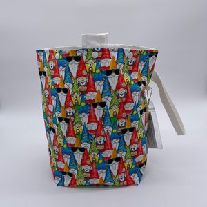 May include: A white canvas tote bag with a drawstring closure and a white handle. The bag is covered in a pattern of colorful gnomes wearing sunglasses.
