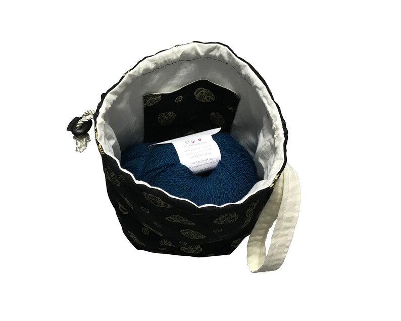May include: A black drawstring bag with a gold floral pattern and a white cotton strap. The bag is open and a teal ball of yarn is inside.