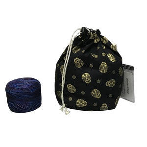 May include: A black drawstring bag with a gold skull pattern and a white drawstring. The bag is filled with a skein of blue and purple yarn.