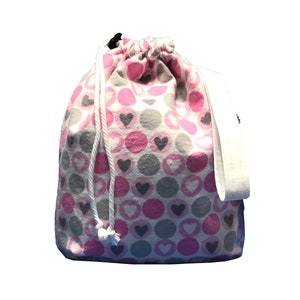May include: A white drawstring bag with a pink and gray polka dot pattern and small hearts. The bag has a white strap.
