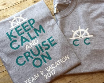May include: Two grey t-shirts with a teal design. One shirt says "Keep Calm and Cruise On" with a ship's wheel graphic. The other shirt has a ship's wheel graphic and the letters "CC". Both shirts say "Team P Vacation 2017".