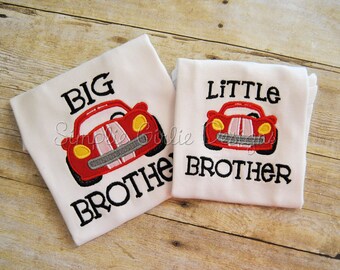 May include: Two white t-shirts with red race car embroidery. The larger shirt says "BIG BROTHER" and the smaller shirt says "LITTLE BROTHER".