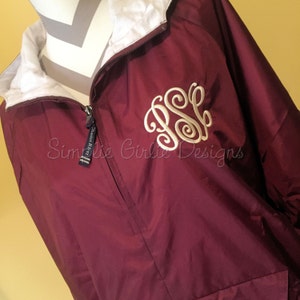 May include: Burgundy windbreaker jacket with a white zip and a white embroidered monogram "JSS" on the front. The jacket has a white lining and a small pocket on the left side.