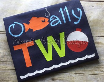 May include: A navy blue t-shirt with the text "O'really Two" in orange, green, and blue. The shirt features a red and white fishing bobber and an orange fish with a fishing hook.