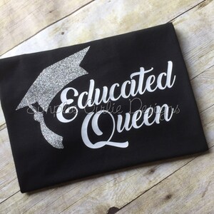 May include: Black t-shirt with a silver glitter graduation cap and the text "Educated Queen" in white.