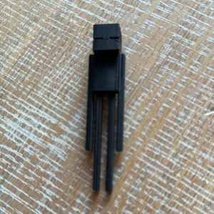 May include: A black 3D printed figurine of a character from the video game Minecraft. The character is standing with its arms outstretched and has a blocky head with a simple face.