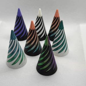 May include: Seven decorative cones with a spiral pattern. The cones are in various colours, including purple, white, copper, green, and black.