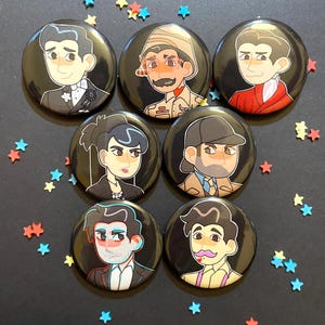 May include: Set of eight round black button pins with colorful cartoon illustrations of people wearing different outfits and hats.
