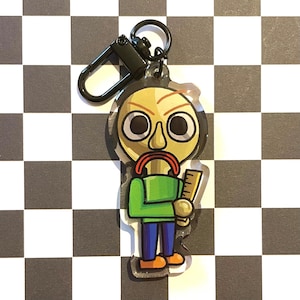 May include: A cartoon-style keychain featuring a character with a bald head, red mustache, and green shirt. The character is holding a ruler and has large, round eyes. The keychain has a black clasp and is set against a checkered background.