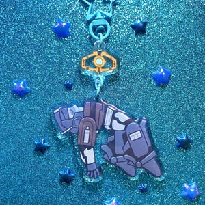 May include: A blue star-shaped keychain with a clear acrylic charm featuring a cartoon character in a blue and gray spacesuit. The charm is hanging from a silver chain and a blue star-shaped clip.
