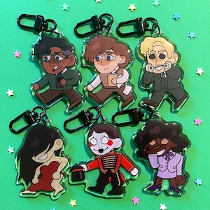 May include: Seven cartoon character keyrings with black clasps. The characters are in various outfits and poses, set against a green background with star-shaped confetti.