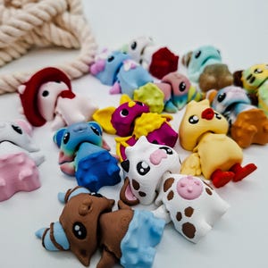Op de afbeelding: Een verzameling kleurrijke, miniatuur dierenfiguren. De figuren tonen verschillende dieren, zoals koeien en vogels, elk met unieke ontwerpen en kleuren. Een beige touw is zichtbaar op de achtergrond.