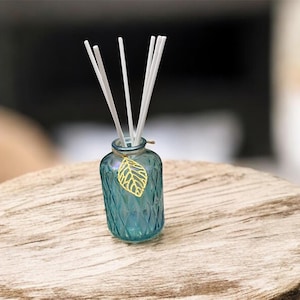 Op de afbeelding: Een blauwe glazen diffuserfles met een bladbedel en witte stokjes. De fles heeft een textuur van een diamantpatroon. De diffuser staat op een houten oppervlak.