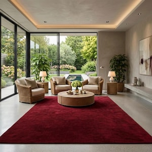 Puede incluir: Un salón moderno con una alfombra roja, sillones de mimbre y una mesa de centro redonda. Grandes ventanales ofrecen vistas a un exuberante jardín y una piscina. La habitación está decorada con tonos neutros y plantas en macetas.