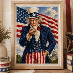May include: A framed cross-stitch embroidery depicting Uncle Sam pointing forward, wearing a top hat and a blue coat with white stars over red and white striped trousers, set against a backdrop of the American flag and the U.S. Capitol building.