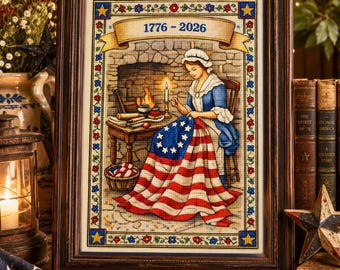 Puede incluir: Un bordado en punto de cruz enmarcado que representa a una persona con vestimenta colonial cosiendo una bandera con trece estrellas en círculo. El texto 1776 - 2026 está centrado arriba. La escena incluye una chimenea de piedra, una mesa y una vela.